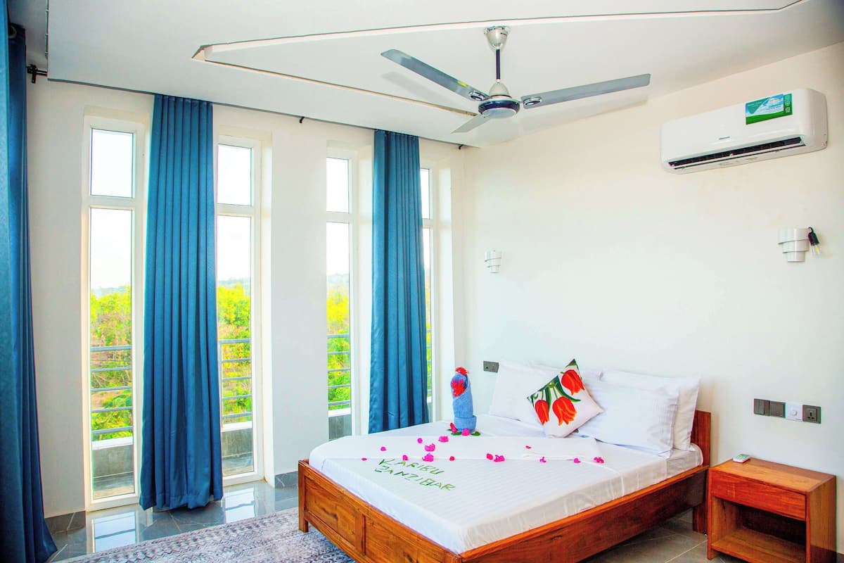 Un dormitorio con cama, ventilador de techo, equipo de aire acondicionado y vistas a través de la ventana.