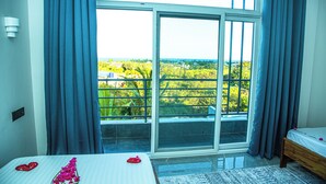 A bedroom with a large window, a bed with a white bedspread, and a view of greenery outside. - Jazira Palace (Pwani Mchangani)