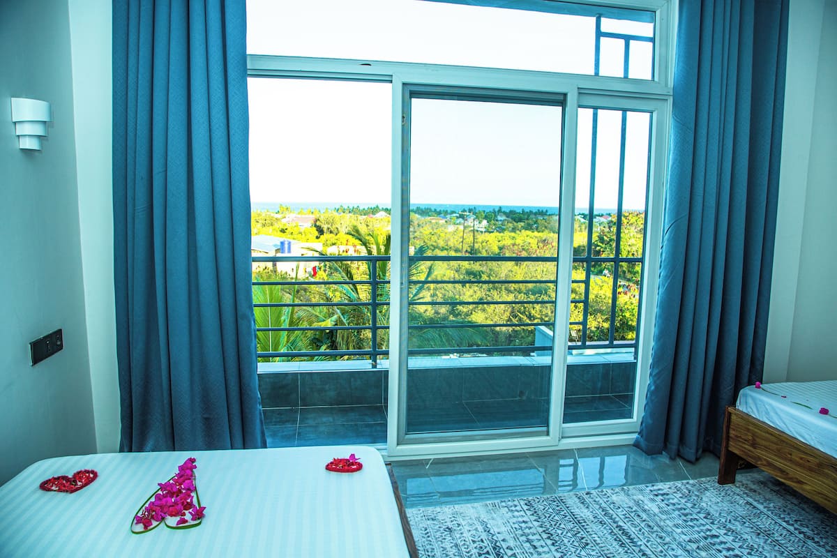 Un dormitorio con un ventanal grande, una cama con cubrecama blanco y vistas a zonas verdes.