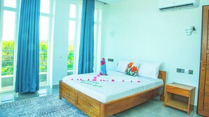 A bedroom with a bed, a nightstand, an air conditioning unit, and a view of greenery outside. - Jazira Palace (Pwani Mchangani)