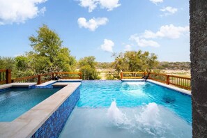 A swimming pool with a wooden deck and a view of the landscape. - Lake House | Pool, Hot Tub, Game Room, Scenic View (Spicewood)