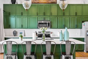 A kitchen with green cabinets, a central island with chairs, and various kitchen appliances. - Lake House | Pool, Hot Tub, Game Room, Scenic View (Spicewood)