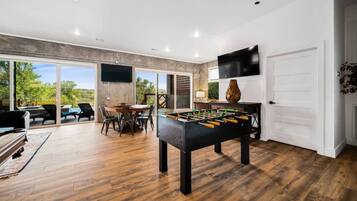 Um quarto espaçoso com mesa de futebol, área de refeições com cadeiras e televisão fixada na parede.