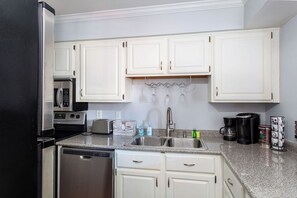 Cozinha com armários brancos, eletrodomésticos de aço inoxidável e bancada de granito.