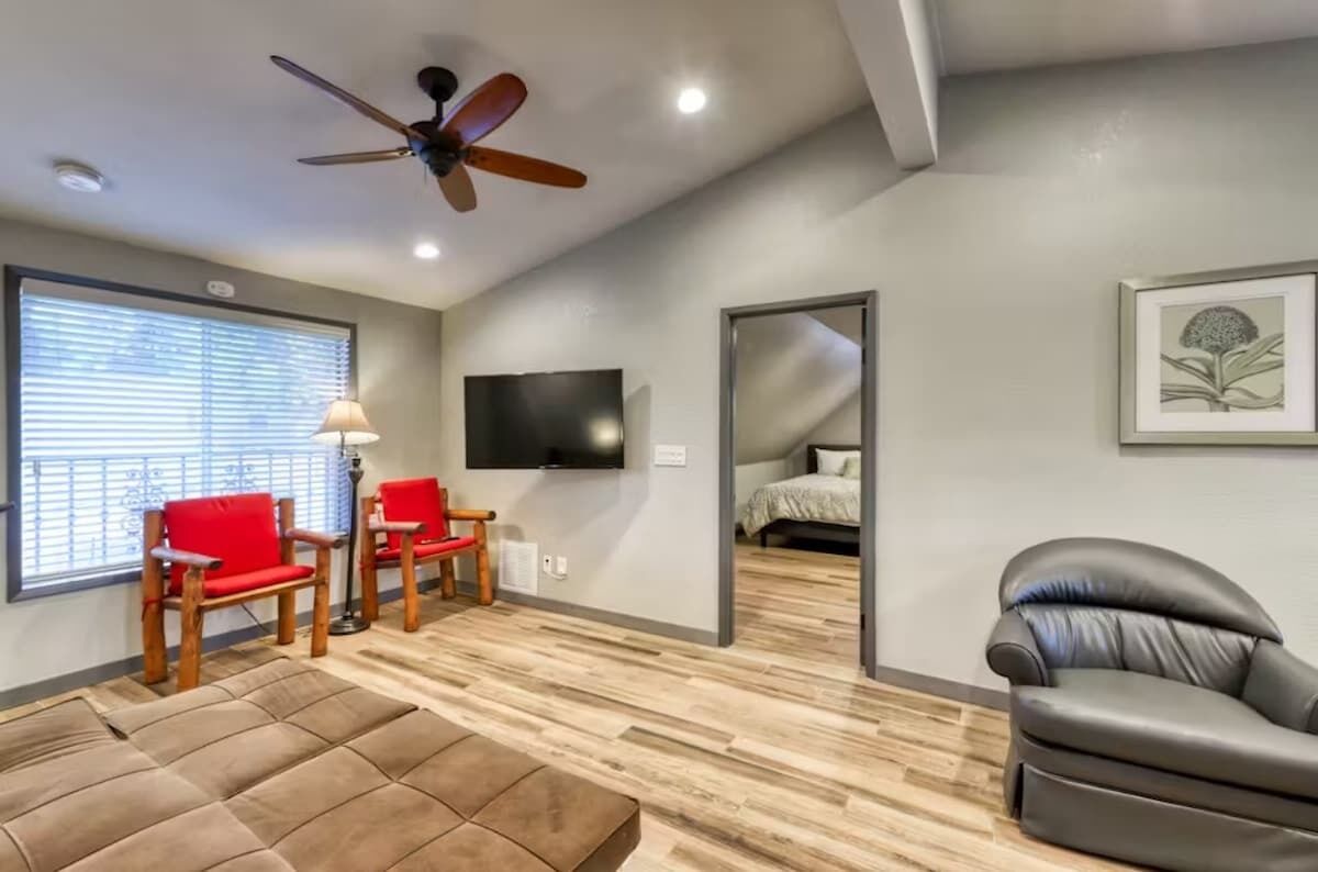 Un salon moderne avec un ventilateur de plafond, un téléviseur, un canapé et un fauteuil rouge.