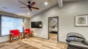 Un salon moderne avec un ventilateur de plafond, un téléviseur, un canapé et un fauteuil rouge.
