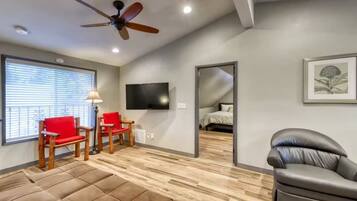 Un salon moderne avec un ventilateur de plafond, un téléviseur, un canapé et un fauteuil rouge.