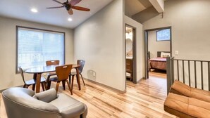 Un espace de vie compact comprenant un coin repas, un canapé, un ventilateur de plafond et une vue sur l’extérieur grâce à une porte ouverte.