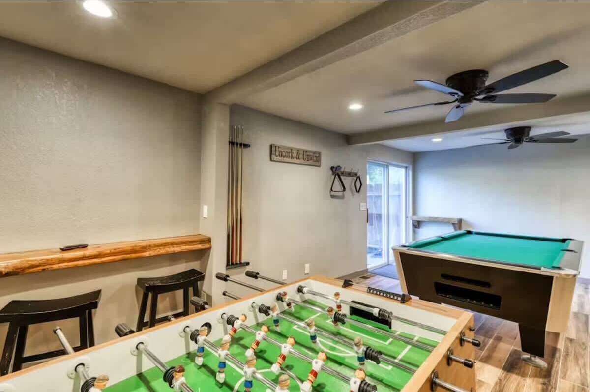 A room with a foosball table, pool table, ceiling fans, and a bar area.