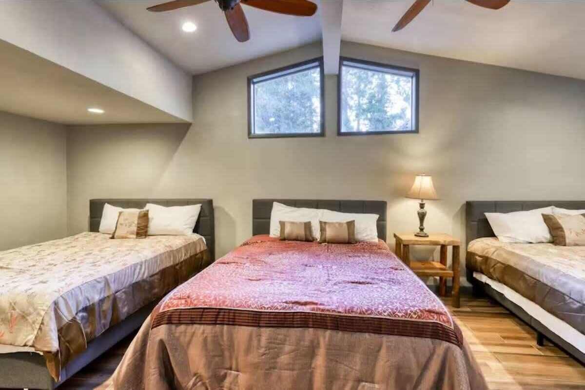 Un dormitorio con tres camas, un ventilador de techo y dos ventanas.