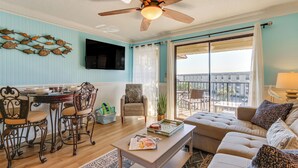 A spacious living room with a ceiling fan, a dining area with chairs and a table, a sofa, and a view of the outdoors through a sliding glass door.