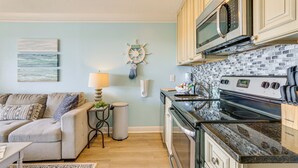 A kitchen with a stove, microwave, and cabinets. There is a small table with a lamp and a trash can.