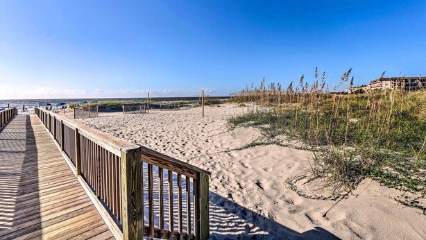 A wooden boardwalk leading to a sandy beach with dunes and vegetation.