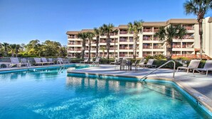 A swimming pool with lounge chairs and a multi-story hotel building in the background.