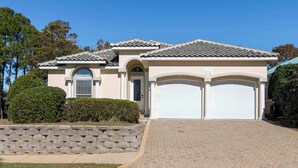 A two-story house with a tiled roof, a stone retaining wall, and a paved driveway. - Gorgeous home with pool and golf cart included! Pet friendly! (Destin)