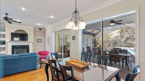 A spacious living area with a glass dining table, comfortable seating, a fireplace, and a view of the outdoor patio. - Gorgeous home with pool and golf cart included! Pet friendly! (Destin)