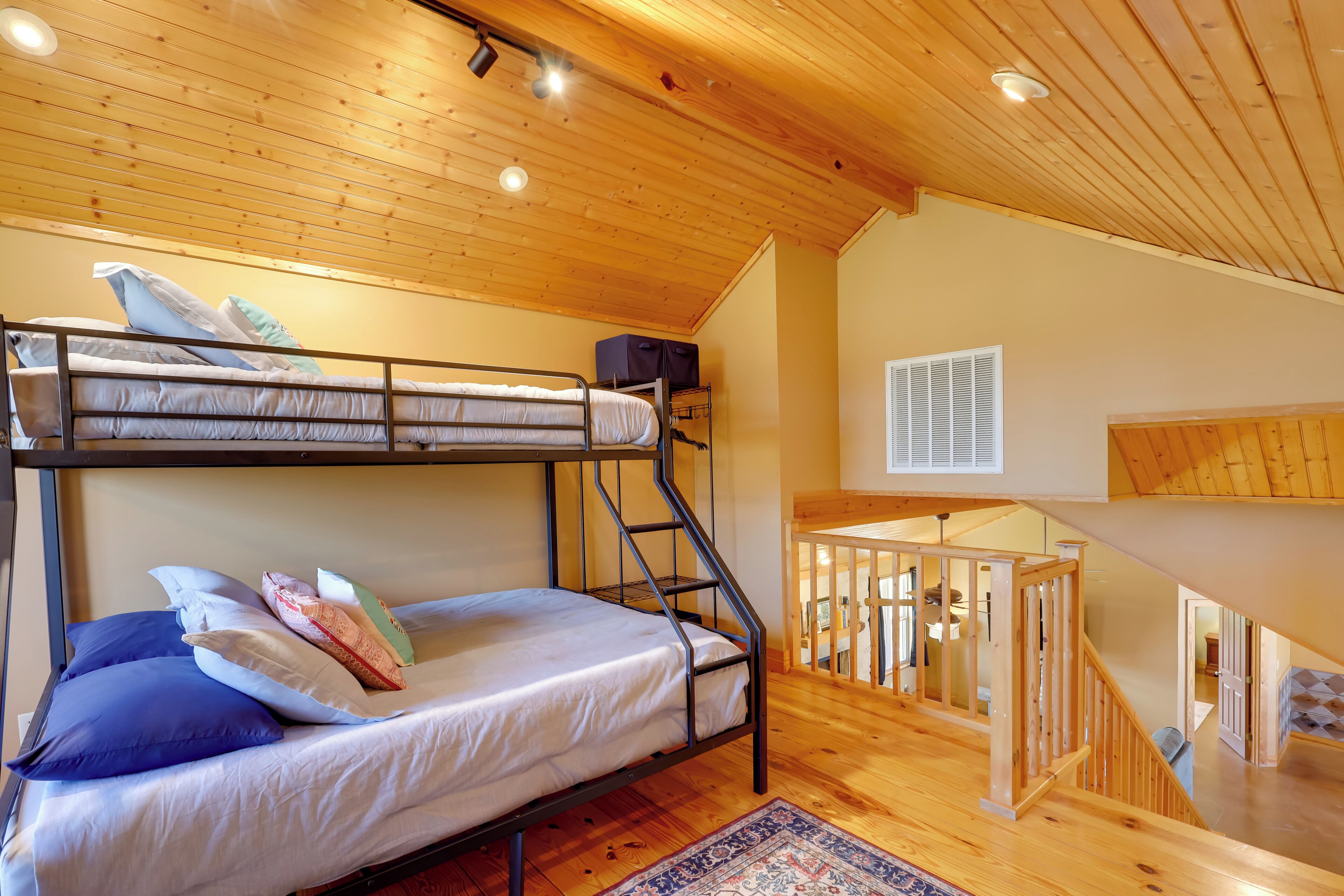 A bunk bed with a wooden ladder, a small desk, and a window with blinds.