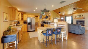 A spacious kitchen with wooden cabinets, a central island with bar stools, a refrigerator, and a fireplace. - Private Hot Tub & Pickleball Court: Baird Home! (Baird)