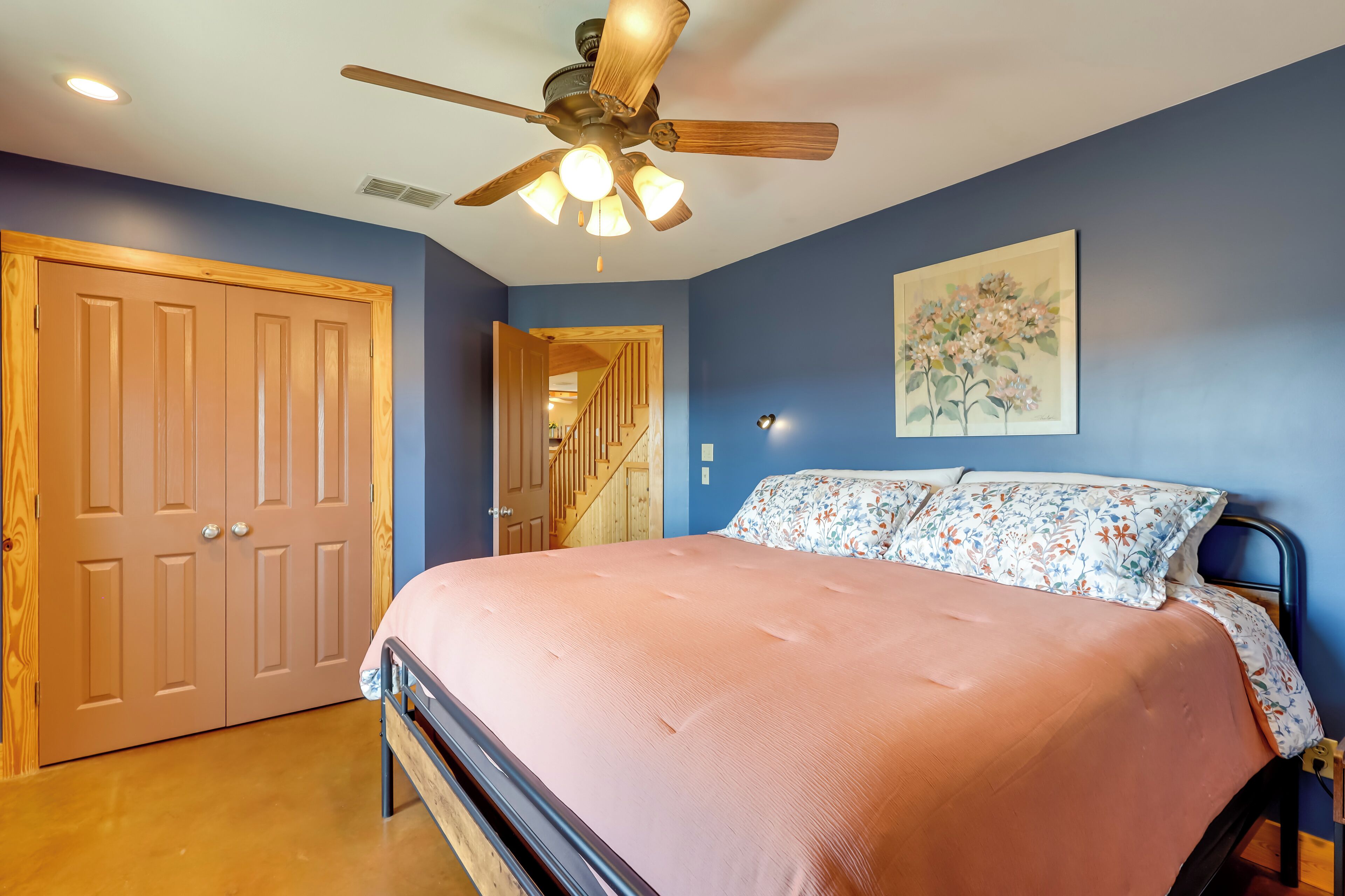 A bedroom with a bed, a ceiling fan, a door, and a staircase leading to another room.