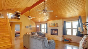 A spacious living room with a large gray sofa, a fireplace, wooden beams, and a ceiling fan. - Private Hot Tub & Pickleball Court: Baird Home! (Baird)