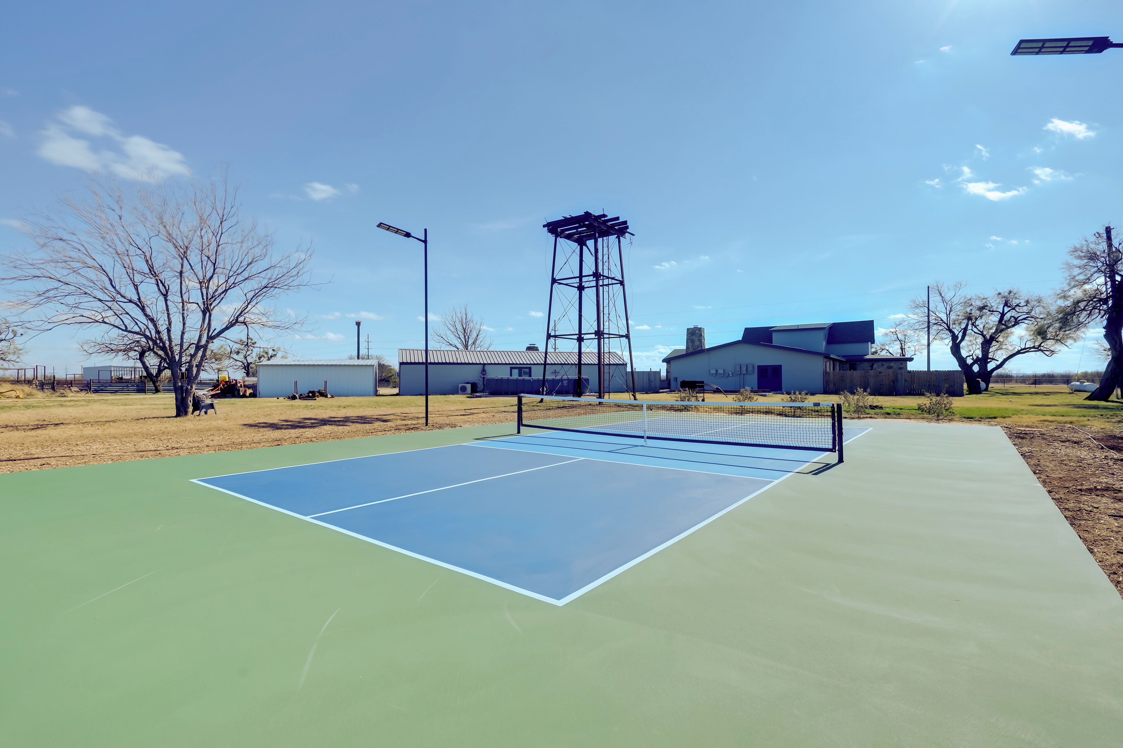 Een tennisbaan buiten met een net, omringd door gebouwen en bomen.