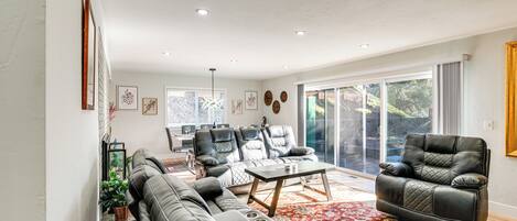 A modern living room with a sectional sofa, a leather armchair, and a coffee table. There is a large window with a view of the outdoors.
