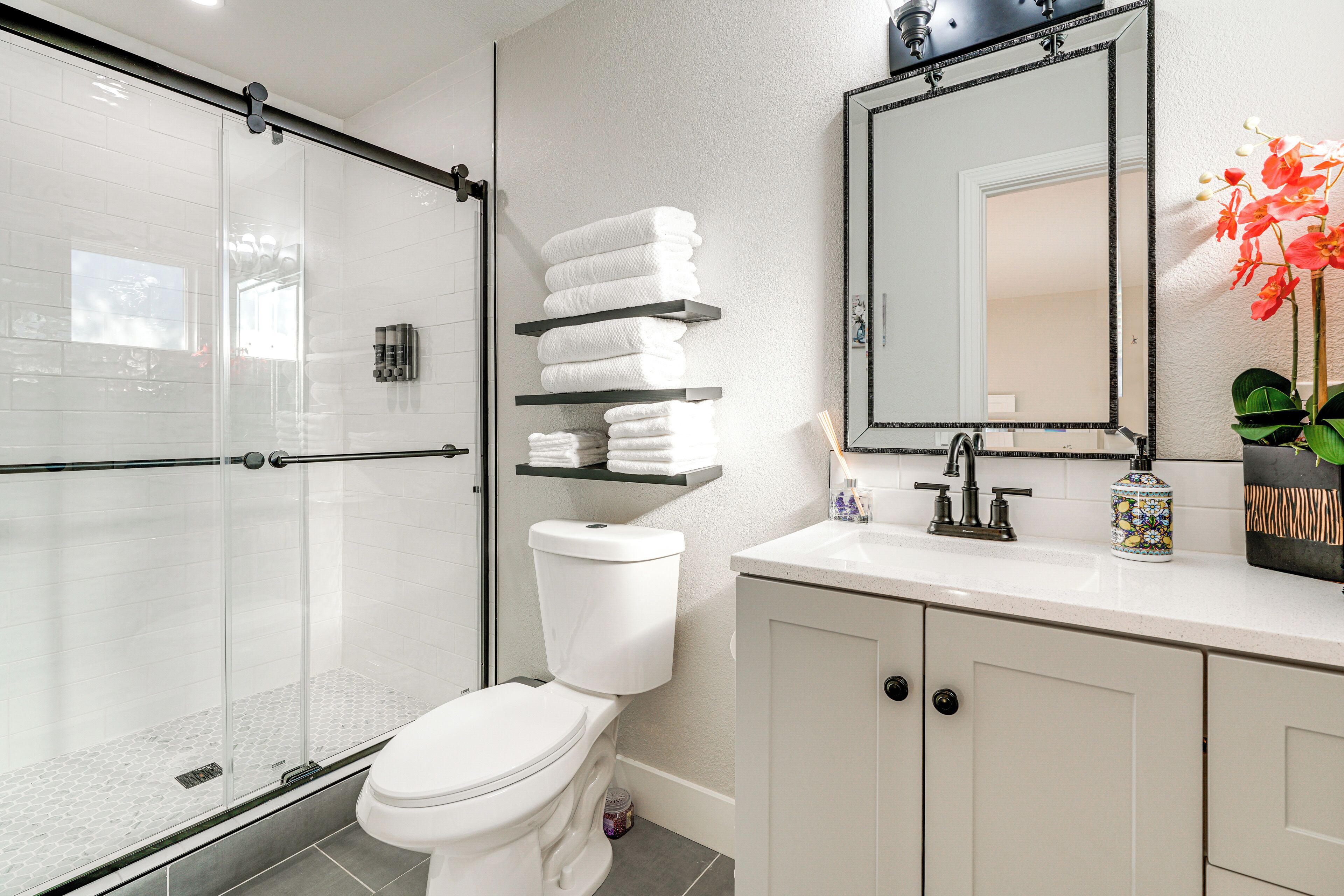 A modern bathroom with a glass shower enclosure, a white toilet, and a vanity with shelves holding white towels.