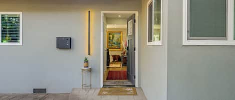 Een moderne entree van een huis met een helder zicht in het interieur, een klein bijzettafeltje met een plant en een deurmat.