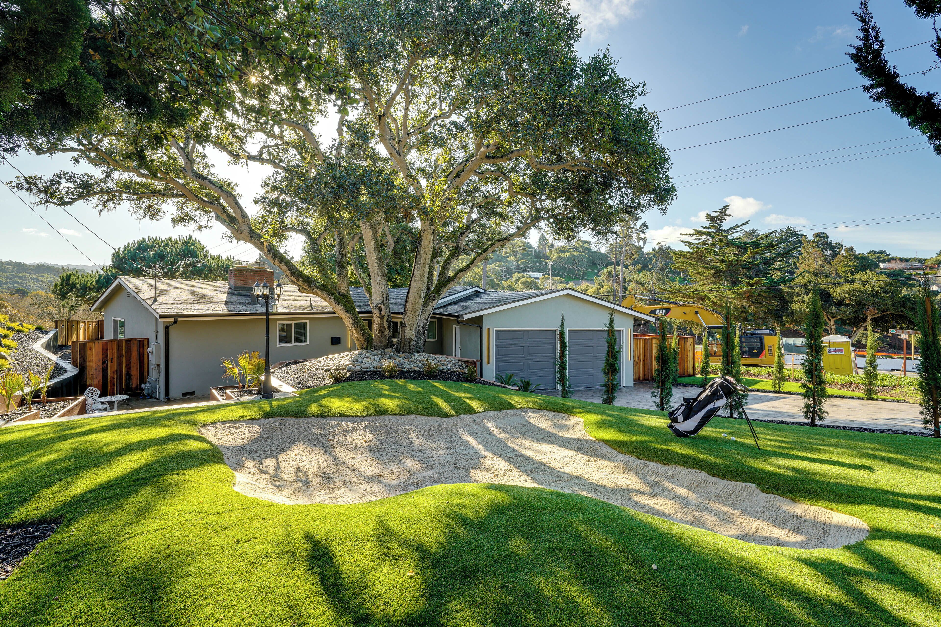 A residential property with a well-maintained lawn, a driveway leading to a garage, and a large tree providing shade.