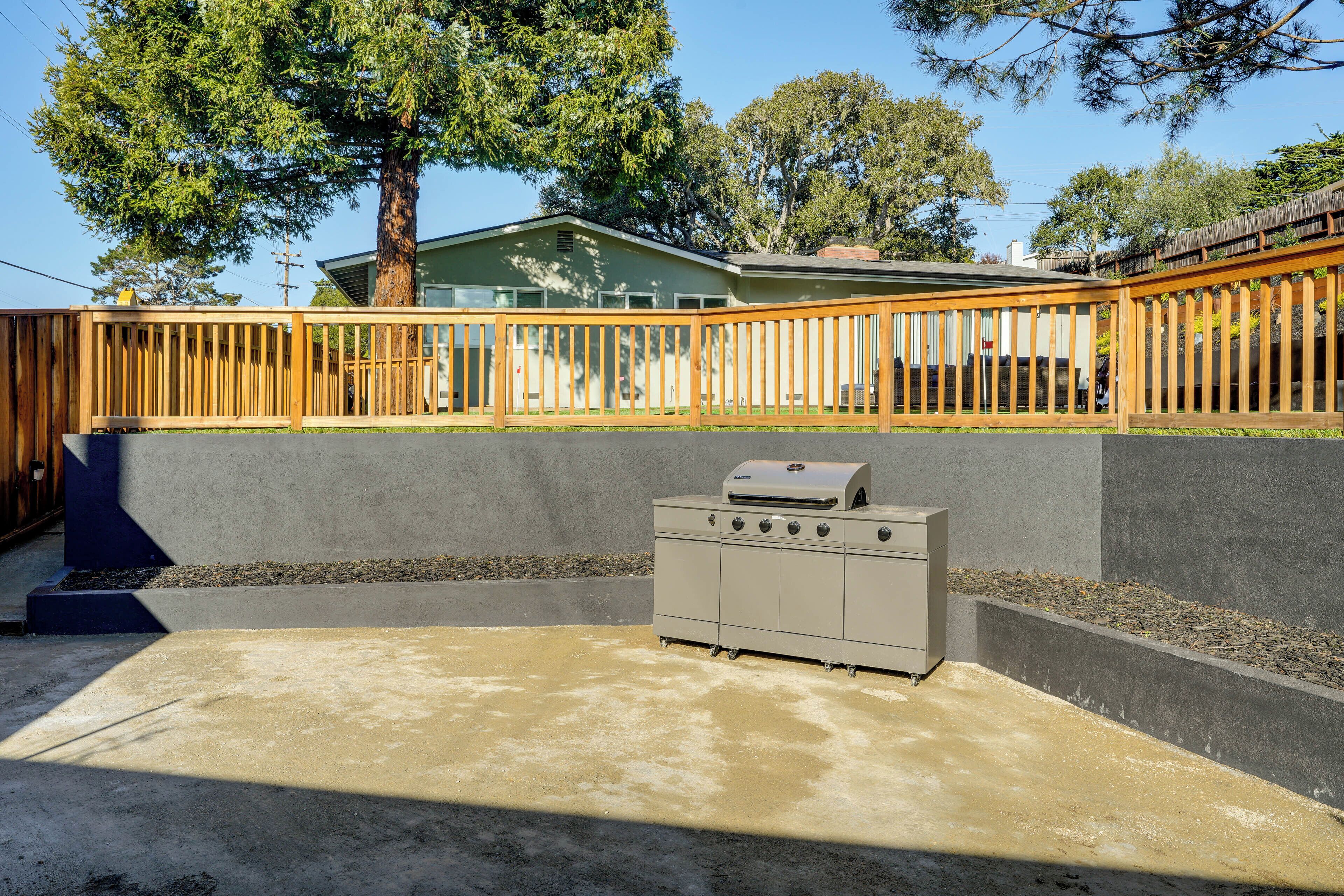 Un patio de concreto con una parrilla, una cerca de madera y una casa al fondo.
