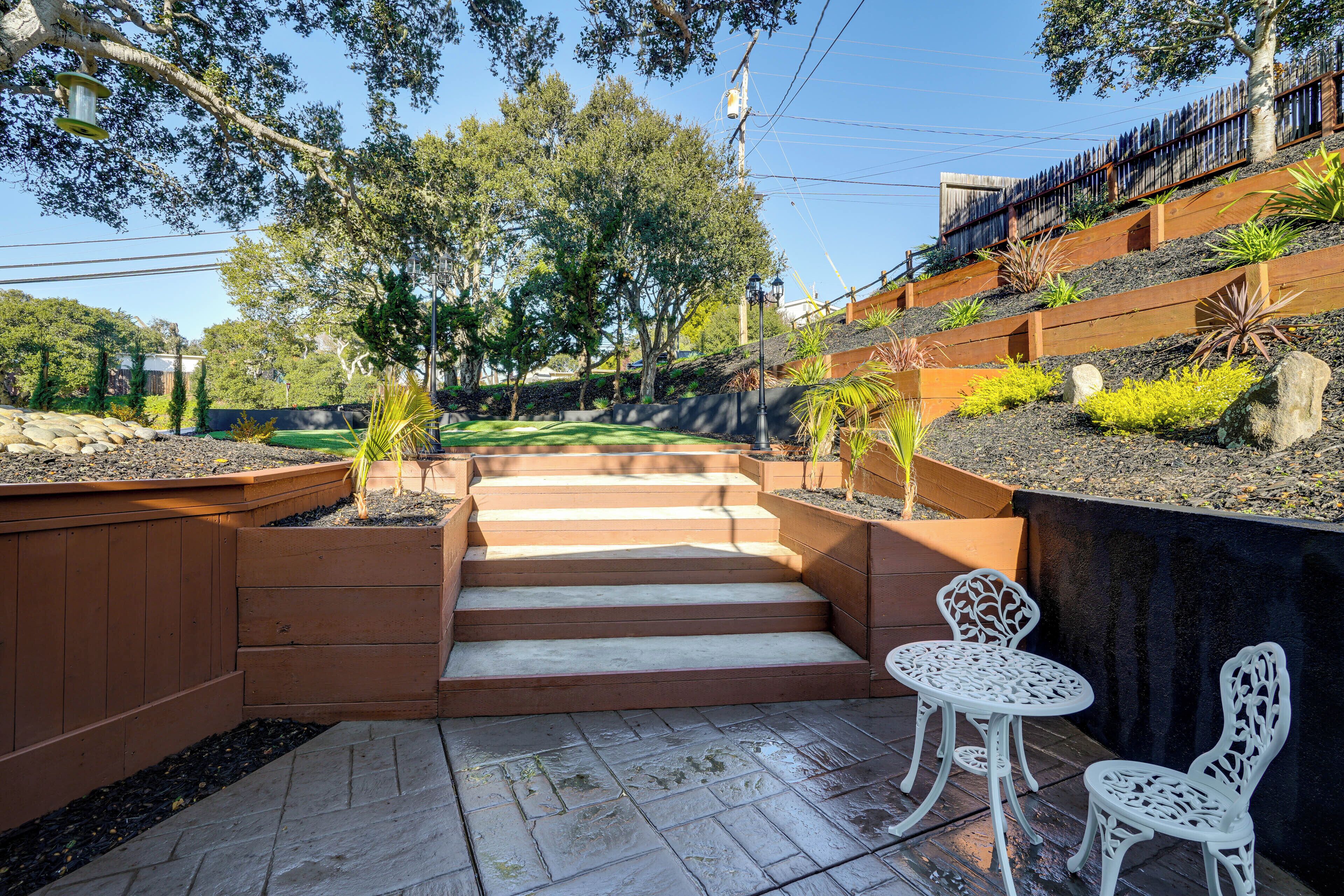 A patio with steps leading to a seating area, surrounded by plants and trees.