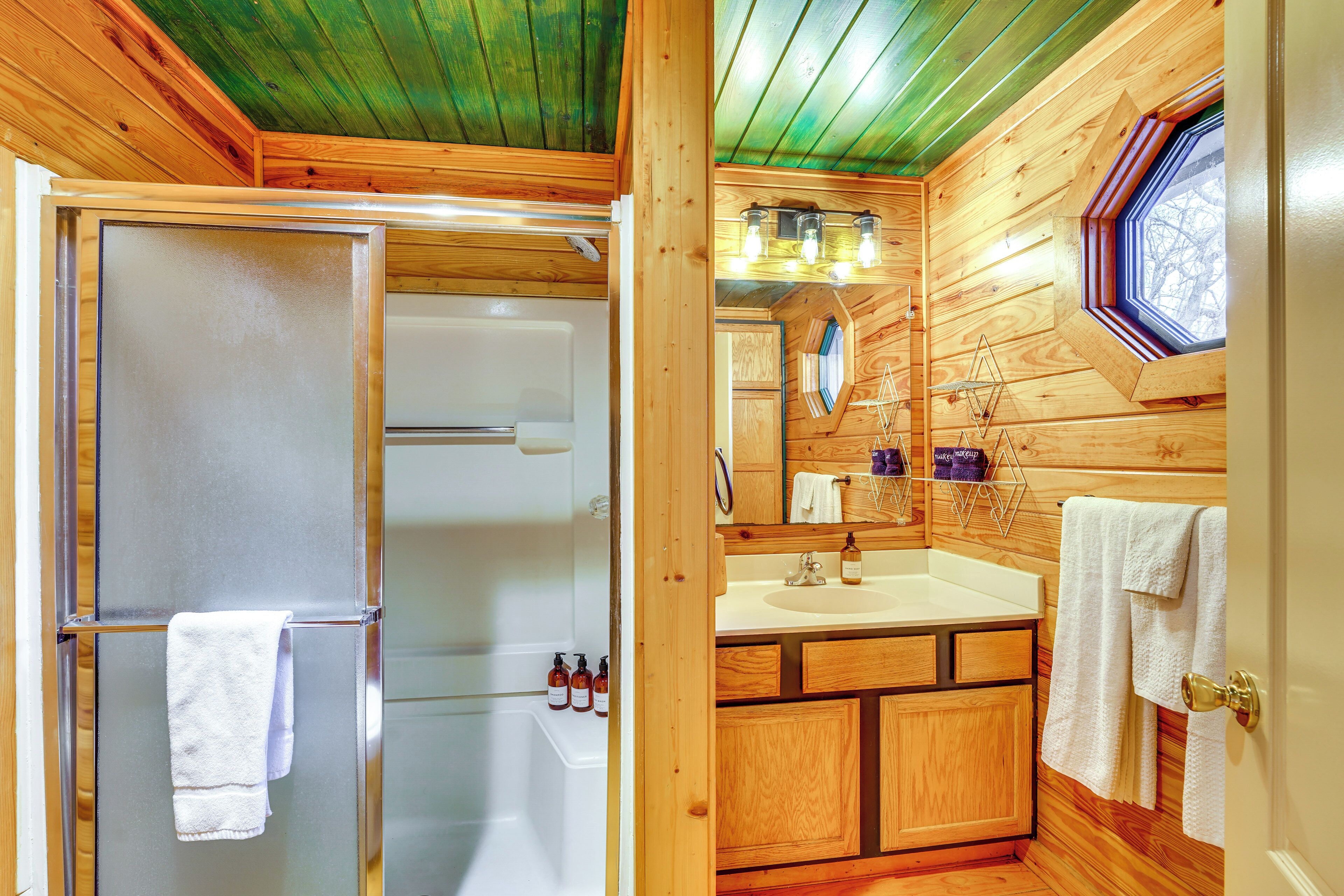 Une salle de bain rustique, avec une cabine de douche en verre, des meubles en bois, un lavabo et une fenêtre offrant une vue agréable.