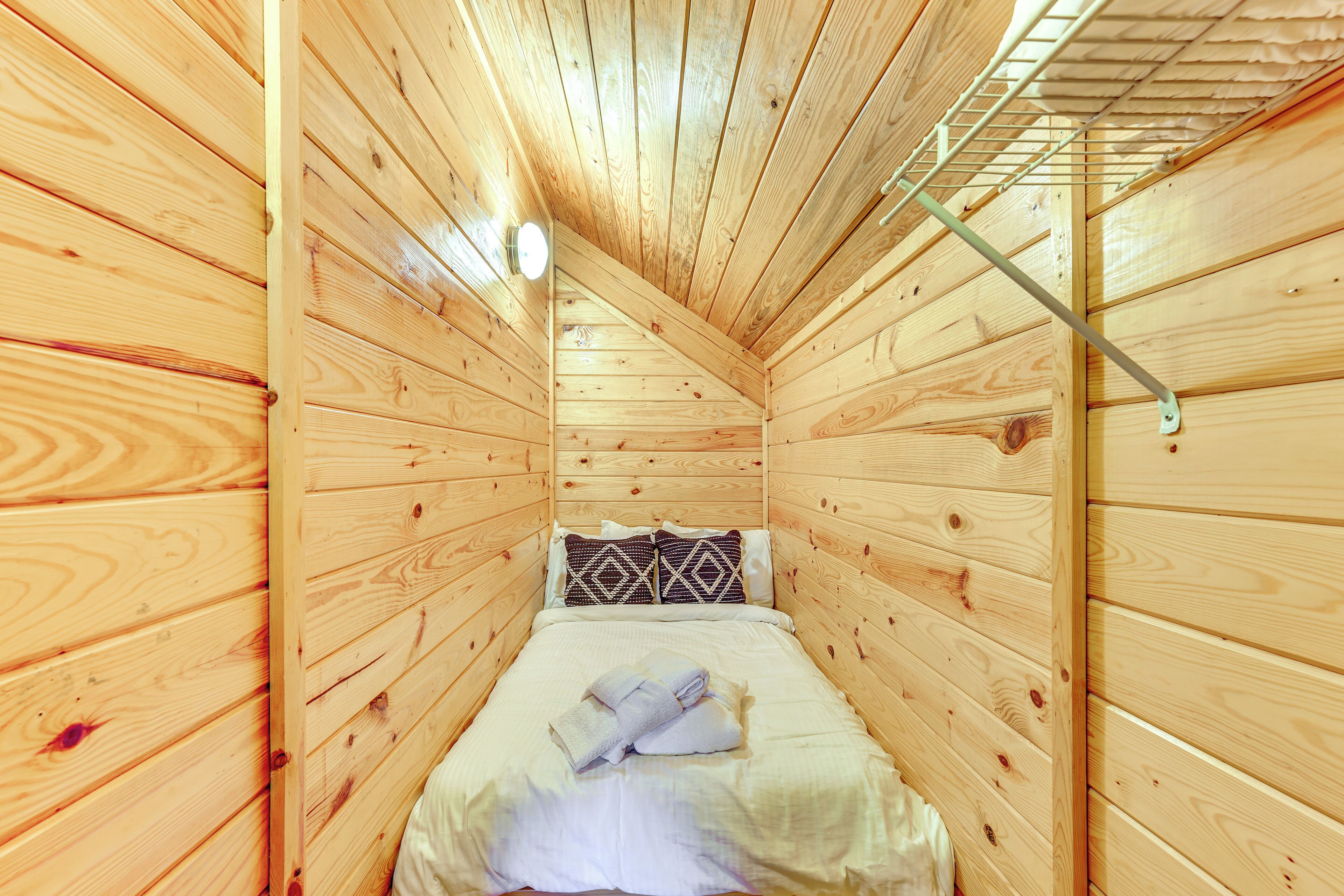 Un pequeño cuarto tipo cabaña de madera con una cama individual, una lámpara en la pared y techo inclinado.