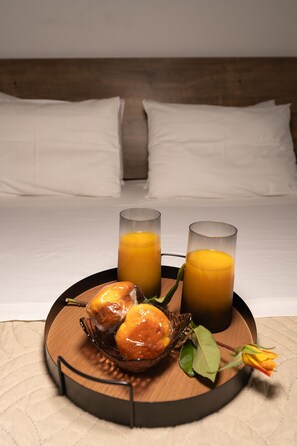 A breakfast tray with two glasses of orange juice, a bowl of fruit, and a rose on a wooden tray in a hotel room.