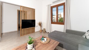 Un salon moderne avec un téléviseur à écran plat, un canapé gris, une table basse en bois et une fenêtre avec des rideaux.