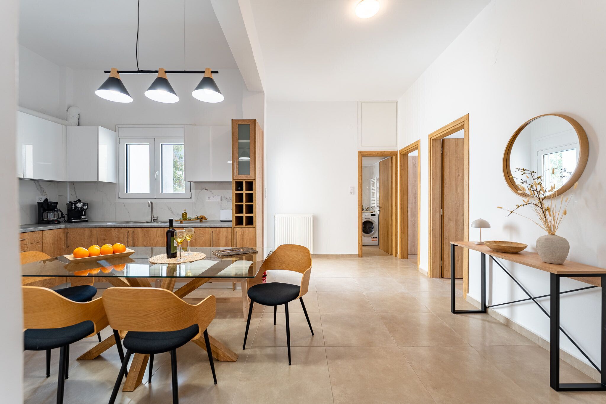 A modern kitchen with white cabinets, a glass dining table, and wooden chairs.