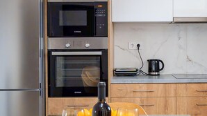 Une cuisine moderne dotée d’appareils électroménagers en acier inoxydable, d’une table à manger en verre avec une bouteille de vin et des verres, et d’armoires en bois.