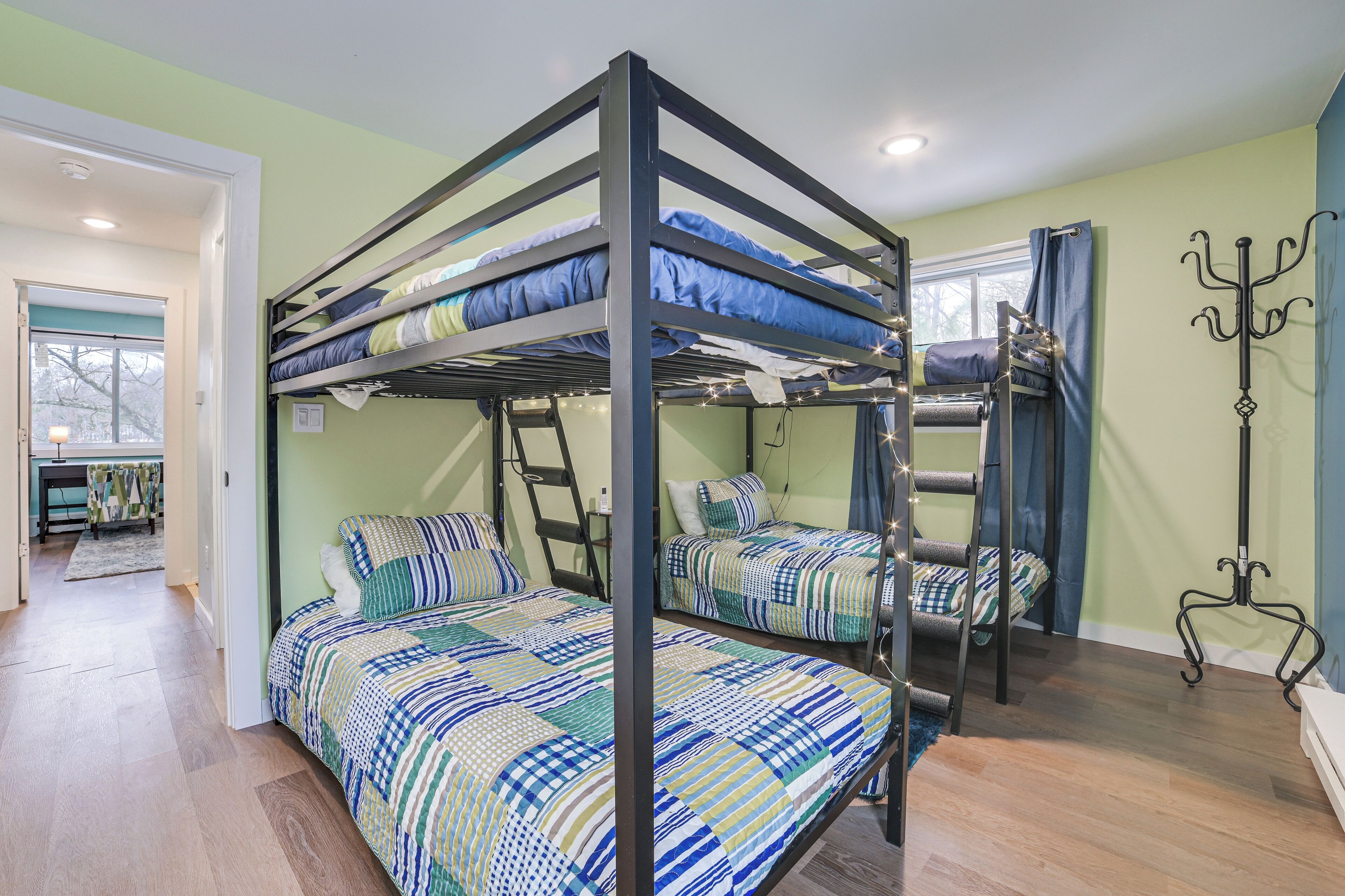 A bunk bed room with a ladder, a coat rack, and a window with curtains.