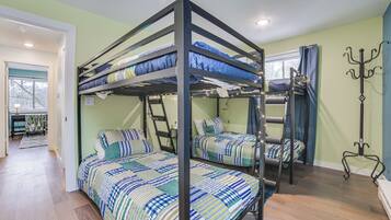 A bunk bed room with a ladder, a coat rack, and a window with curtains.