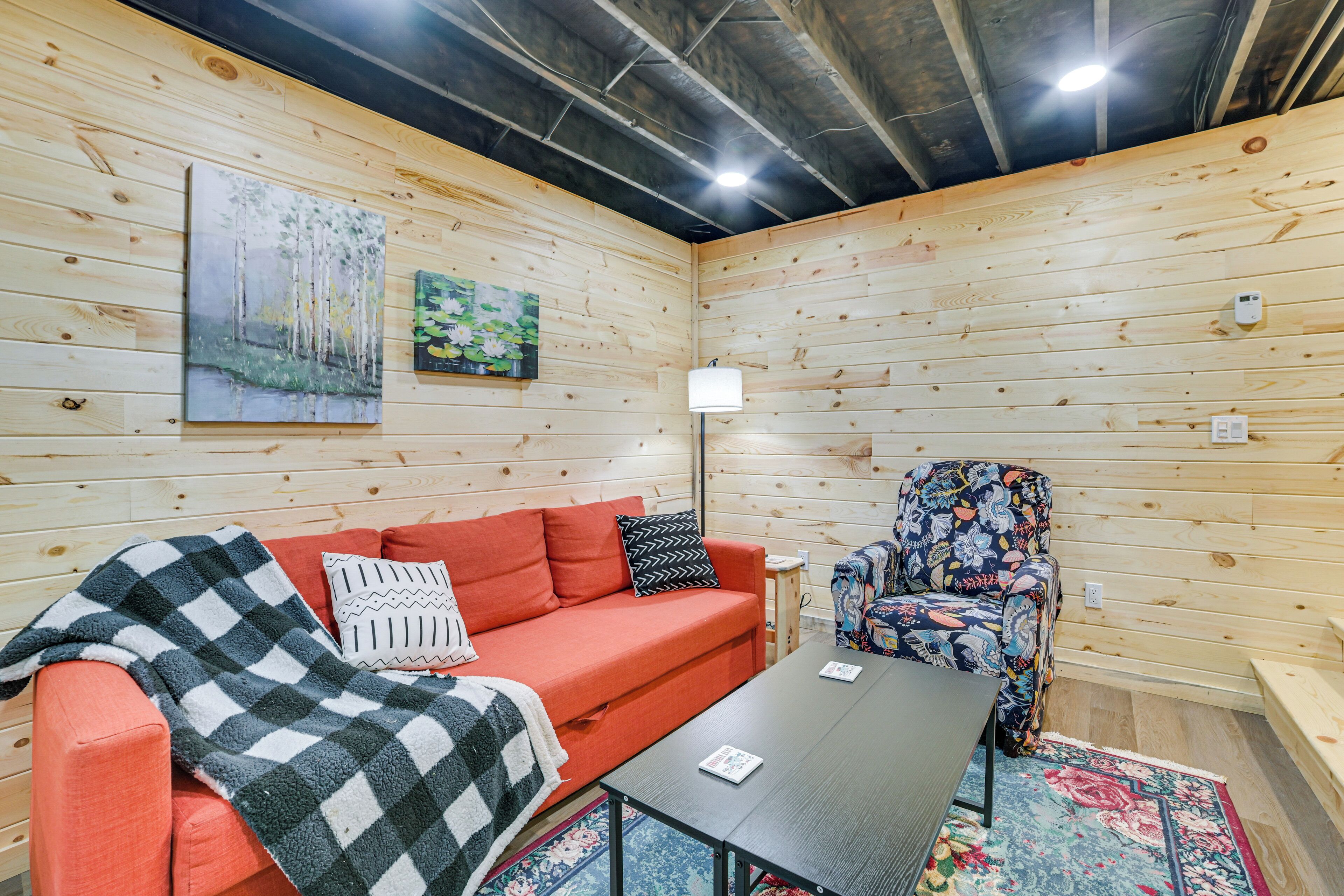 A cozy room with a wooden interior, a red sofa, a patterned armchair, and a small table.