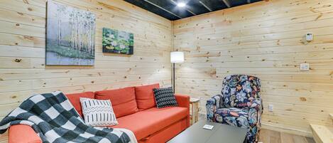 A cozy room with a wooden interior, a red sofa, a patterned armchair, and a small table.