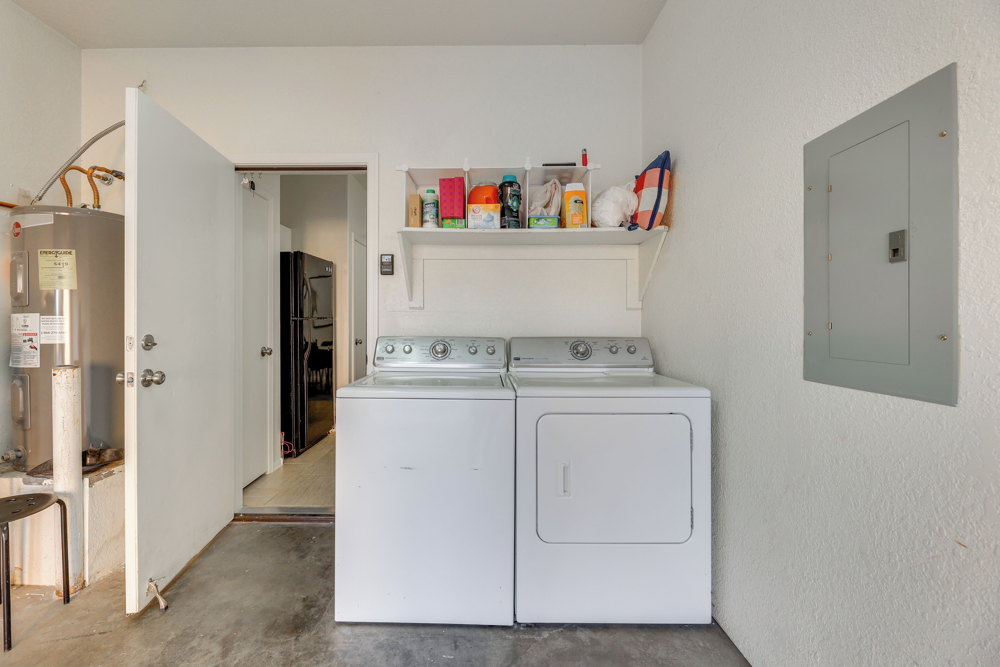 A laundry room with a washer and dryer, a shelf with cleaning supplies, and a door leading to another room.