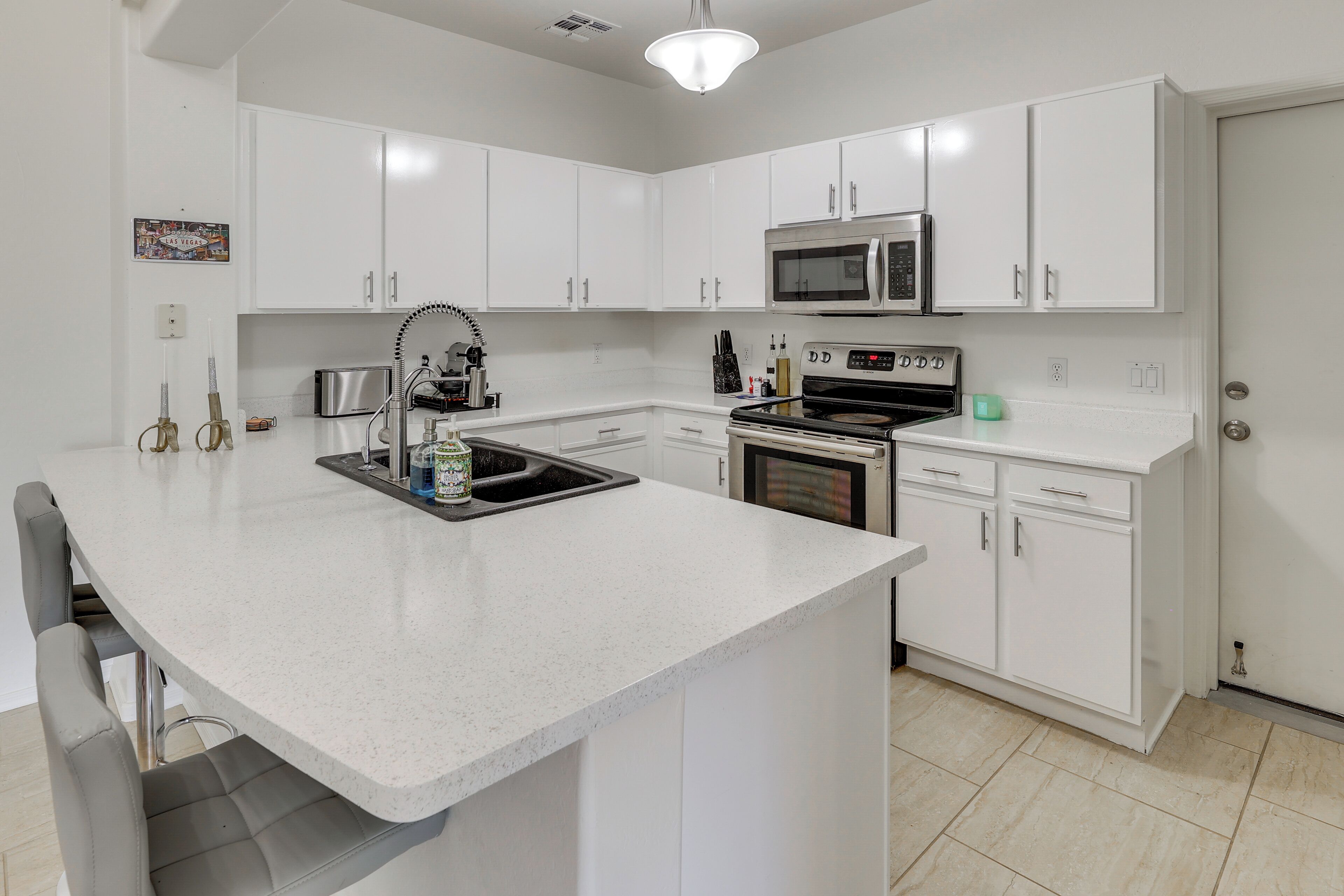 A modern kitchen with white cabinetry, a central island, stainless steel appliances, and a pendant light.
