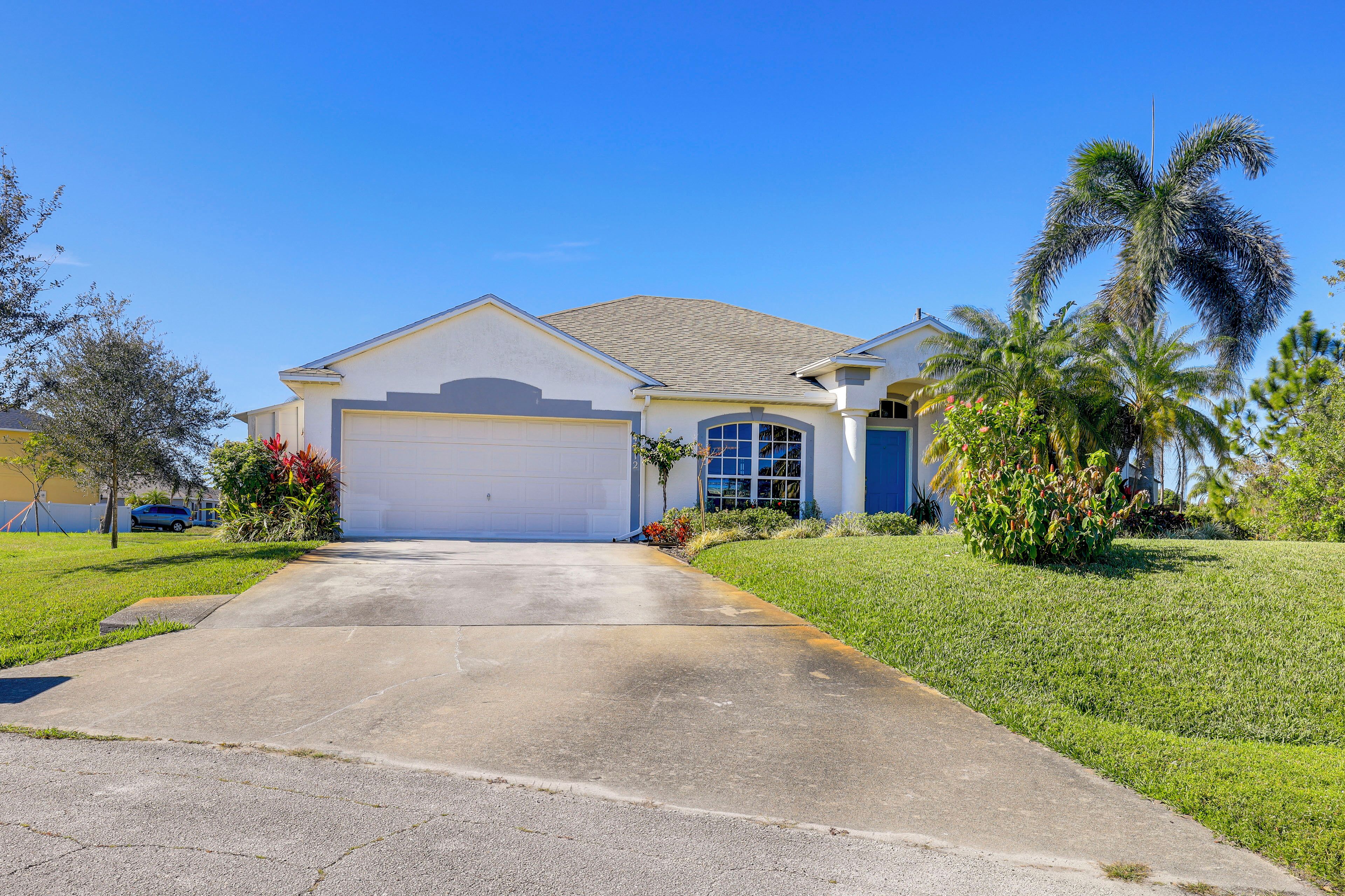 A single-story house with a garage, a well-maintained lawn, and a palm tree.
