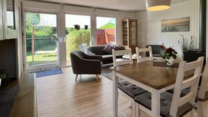 Amplia sala de estar con una mesa de comedor de madera, sillas blancas, un sofá y un gran ventanal con vistas al exterior.