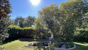 Un jardín cuidado con un sendero de piedra circular, una pequeña estructura blanca y abundante vegetación.