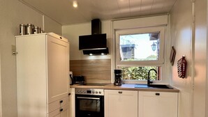 Una cocina compacta con gabinetes blancos, horno empotrado, cafetera y ventana con vista a zonas verdes.