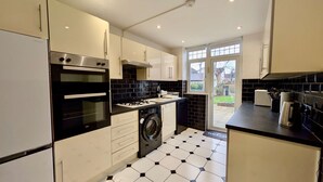 Een moderne keuken met een zwart-wit betegelde vloer, roestvrijstalen apparatuur en uitzicht op de achtertuin door een glazen deur.