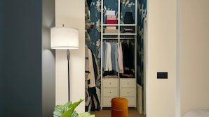 Un dormitorio con armario, lámpara de pie, planta y un pequeño reposapiés.