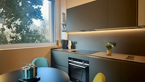 Una cocina moderna con horno empotrado, una mesa de comedor con sillas y un ventanal con vistas a árboles.